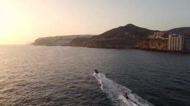 Kayalık sahil boyunca yüzen eğlence tekneleri, gün batımında kıyı şeridini gören hava manzarası. Büyük Kanarya. İspanya.