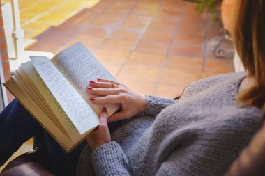 Beyaz kadın koltukta kitap okuyor dışarıda gün ışığında rahatlıyor. Uzayı kopyala Okuma, öğretme konsepti. Arkaplan.