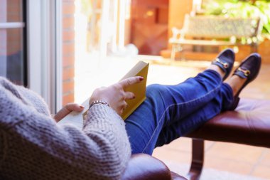 Beyaz kadın koltukta kitap okuyor dışarıda gün ışığında rahatlıyor. Uzayı kopyala Okuma, öğretme konsepti. Arkaplan.