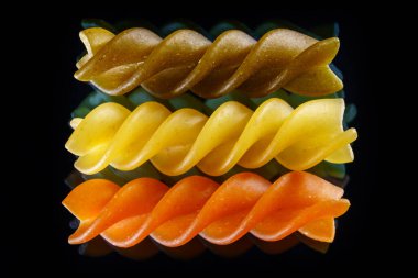 Siyah arka planda pişmemiş üç renkli makarna. Makro yemek fotoğrafı..