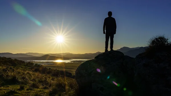 Sırtı dağların üzerinden gün batımına bakan bir adam bir kayanın üzerinde duruyor. Navacerrada Madrid 'de. İspanya.