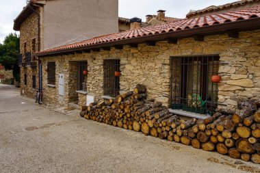 Firewood stacked on the facade of an old house made of stone and bicycle parked at the entrance. Madrid.