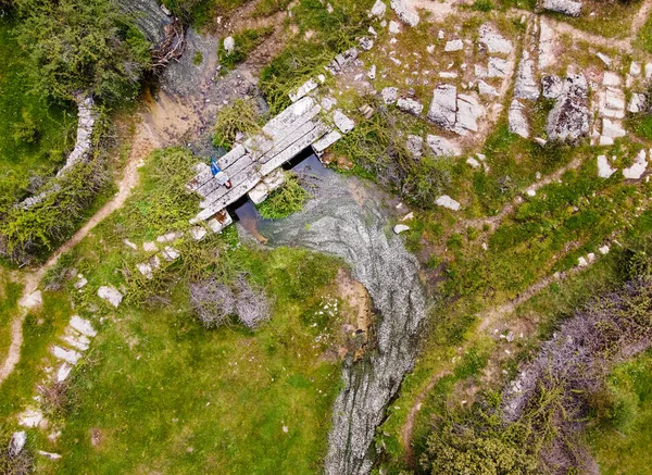 Yeşil tarladaki eski taş köprüde yatan kadının hava görüntüsü. İspanya.
