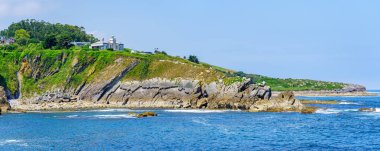 Panoramic of a lighthouse on top of a cliff next to the sea in sunny day. Suances Santander. clipart