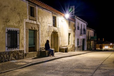 Geceleri antik bir köyde taş bir bankta oturan bir kadın..