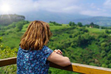 Yeşil vadiyi, ufukta güneşin parıltılarıyla gören bir kadın. Santander.