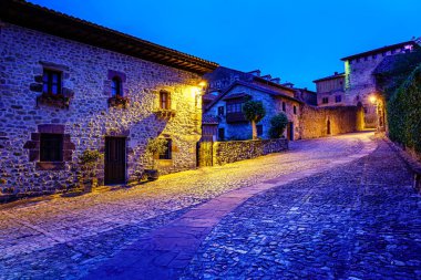 Cobbled caddesi ve alacakaranlıkta kilise kulesi olan resim gibi bir ortaçağ sokağı. Santillana del Mar.