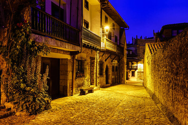 Picturesque street of stone houses with balconies and streetlight lights at night.