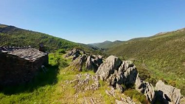 Madrid dağlarında baharda çiçeklerle ve kaya oluşumlarıyla kaplı yeşil bir çayırdaki küçük yüksek dağ evi.