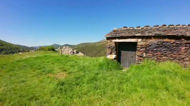 Madrid dağlarında baharda çiçeklerle ve kaya oluşumlarıyla kaplı yeşil bir çayırdaki küçük yüksek dağ evi.
