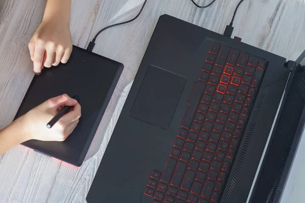 A person draws with a pen on a graphics tablet in front of a laptop.