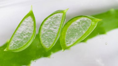 Şeffaf arkaplanda su ve meyve suyu damlalarında şeffaf yeşil aloe vera yaprağı dilimleri.