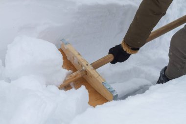 Bir adam kışın tahta bir kürekle karı temizler.