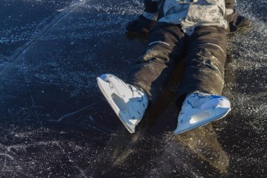 Beyaz paten giyen bir çocuk kışın bacaklarını esnetirken nehrin buzunda oturur..