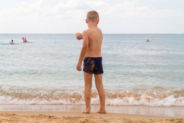 Yazın beyaz bir çocuk sahilde durur ve okyanusa çakıl taşları atar.