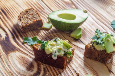 Kahverengi ahşap bir masada yeşil filizlenmiş karabuğday, avokado, maydanoz ve çavdar ekmekli sandviç..