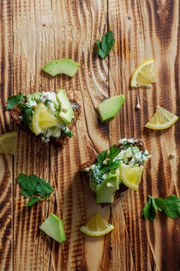 Yeşil lahanalı sandviçler, avokado, maydanoz, limon dilimleri ve kahverengi ahşap bir masada çavdar ekmeği. Üst görünüm, arkaplan, kopyalama alanı.