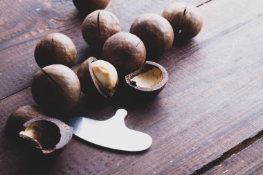 Kahverengi ahşap bir masada Macadamia fındıkları. Macadamia fındığı açmak için özel metal anahtar.