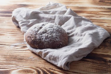 Bej peçete ve ahşap arka planda yuvarlak şekilli koyu çavdar ekmeği..