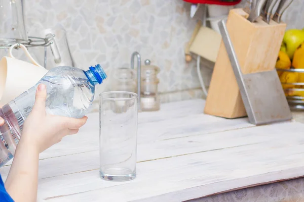 Pour water into a glass glass from a plastic bottle in the kitchen at home.