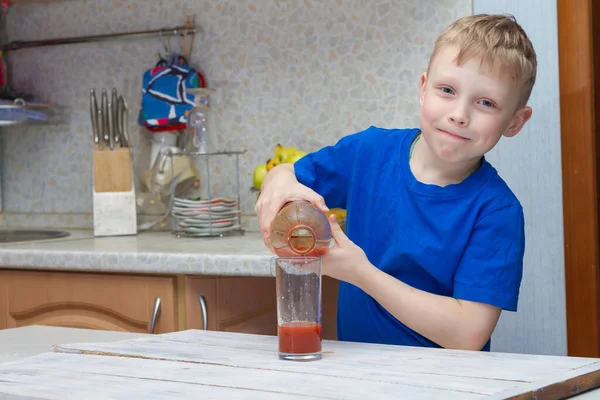 一个男孩从厨房的瓶子里往杯子里倒番茄汁 — 图库照片