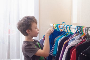 Çocuk kıyafetlerini gardıroptaki askılara asıyor..