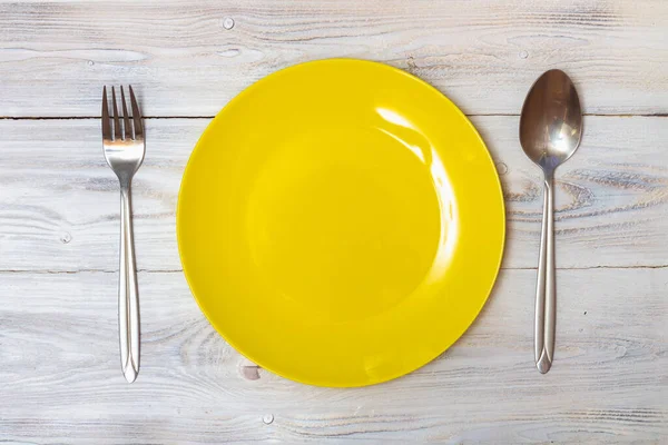 Un plato amarillo vacío con una cuchara y un tenedor sin comida está sobre una mesa blanca —  Fotos de Stock