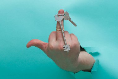 Delikten geçen mavi olanın üzerinde parmaklarınla dünyanın jestini göster. Parmağında bir evin ya da dairenin anahtarları..