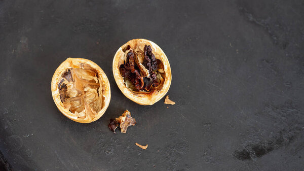An empty walnut shell with a dried walnut kernel on a black background.