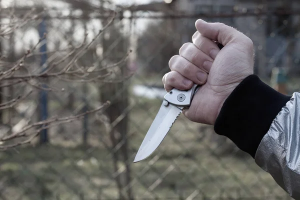 A knife in the hand of a man with a sharp steel blade in the park as a weapon or a means of self-defense.