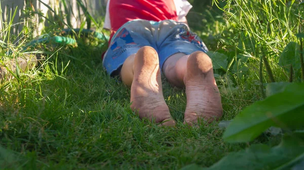 a child with dirty feet lies on the grass in the summer.