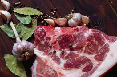 Bir parça çiğ domuz eti ve bezelye, defne yaprağı, kahverengi ahşap arka planda sarımsak..