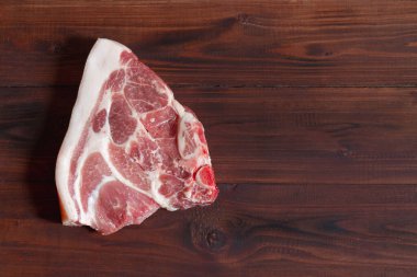 Kahverengi ahşap zemin üzerinde yağ ve kemik katmanları olan bir parça taze domuz boynu eti. Boşluğu kopyala.