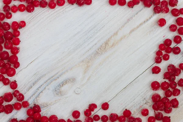 stock image Frozen red currant on a white wooden background in the form of a frame on the edge.