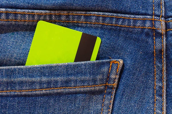 A plastic discount card or a light green bank card in the pocket of blue jeans.