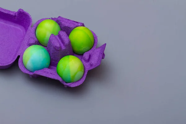 Œufs de Pâques dans une boîte à œufs en carton violet sur fond gris pour les vacances de Pâques. Espace de copie — Photo