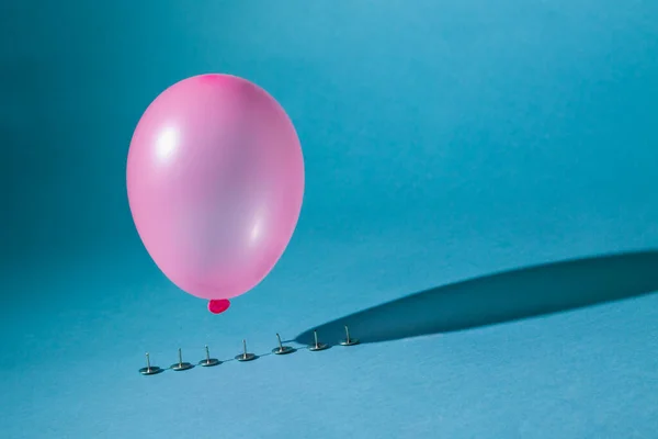 Globo Rosa Cae Sobre Botones Metálicos Afilados Sobre Fondo Azul — Foto de Stock