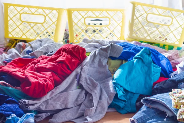 A pile of un-ironed clothes of different colors is lying on the floor for sorting into storage containers for clothes.