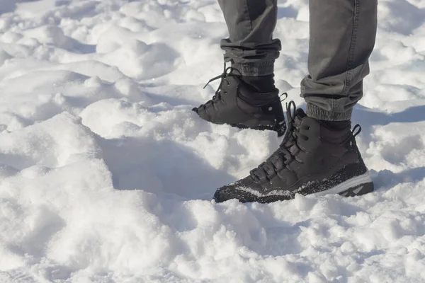 The feet of a man in winter warm shoes on the snow in a frosty winter.