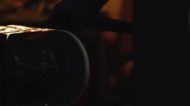 Metalin keskinleştirilmesinden kıvılcımlar uçuşuyor. Öğütme makinesinin dönen çarkının baltasını bileyin