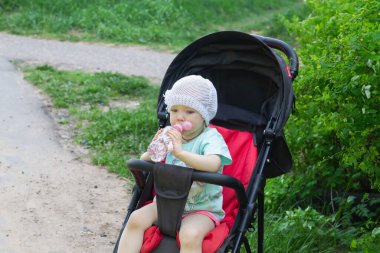 Bebek kız yazın sıcağın altında bebek arabasında otururken plastik şişeden su içer..