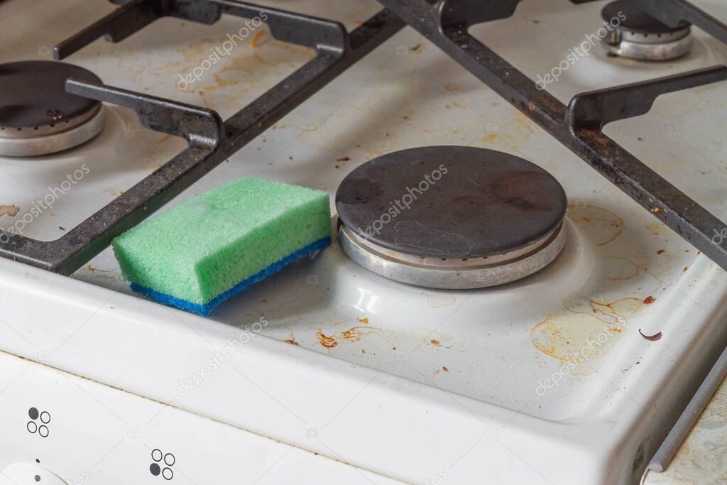 Dirty stove in the kitchen with a cleaning sponge with detergent. Cleaning the gas stove at home.