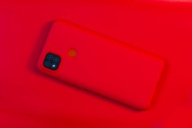 Kırmızı arka planda silikon bir çantada kırmızı akıllı telefon.