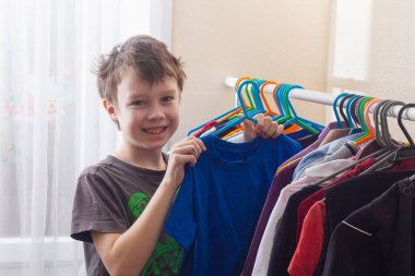 Çocuk kıyafetlerini gardıroptaki askılara asıyor..