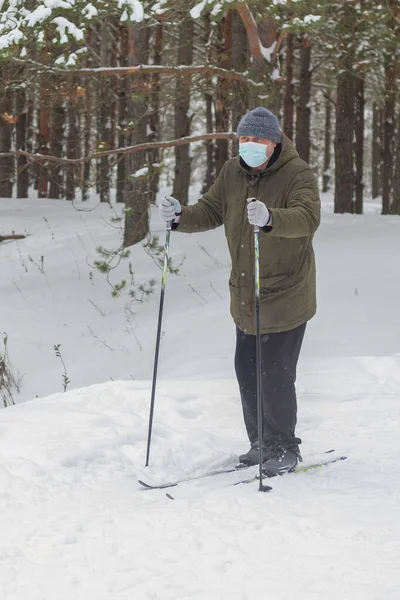 A strange man wearing a medical mask to protect himself from the virus walks through the forest on skis in winter.