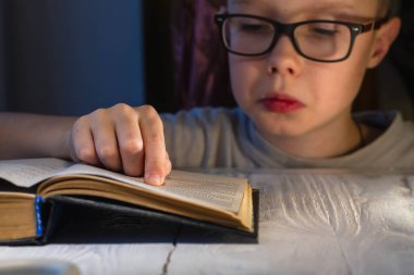 Gözlüklü genç bir beyaz çocuk kitap okumakta zorlanıyor ve metni anlamlandırmaya çalışıyor..