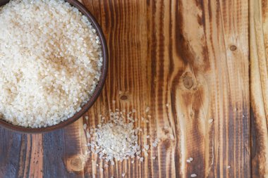 Kahverengi ahşap bir masada yuvarlak pirinçli kahverengi kilden bir kase..