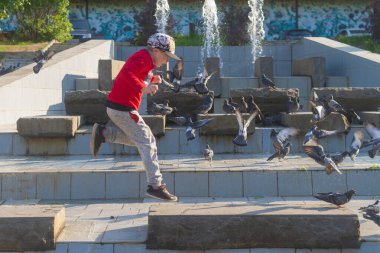 Bir çocuk yazın parkta çeşmenin üzerindeki fayansların üzerine atlar..