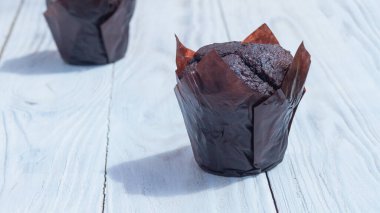 Yumuşak hamurdan yapılmış lezzetli çikolatalı kekler beyaz ahşap bir masada kağıda sarılır.