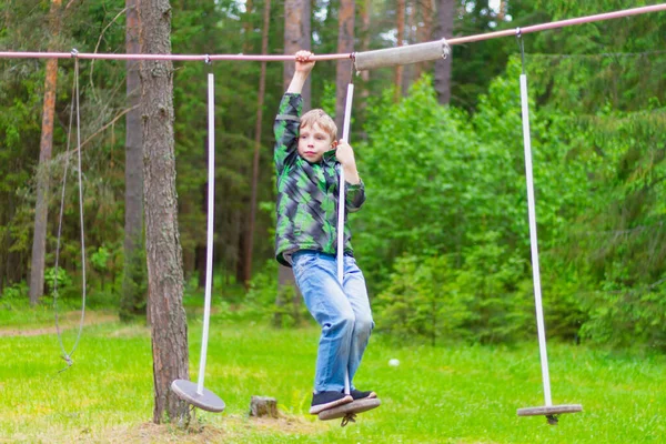 En pojke övervinner hinder i ett rep spår i skogen på sommaren eller våren — Stockfoto